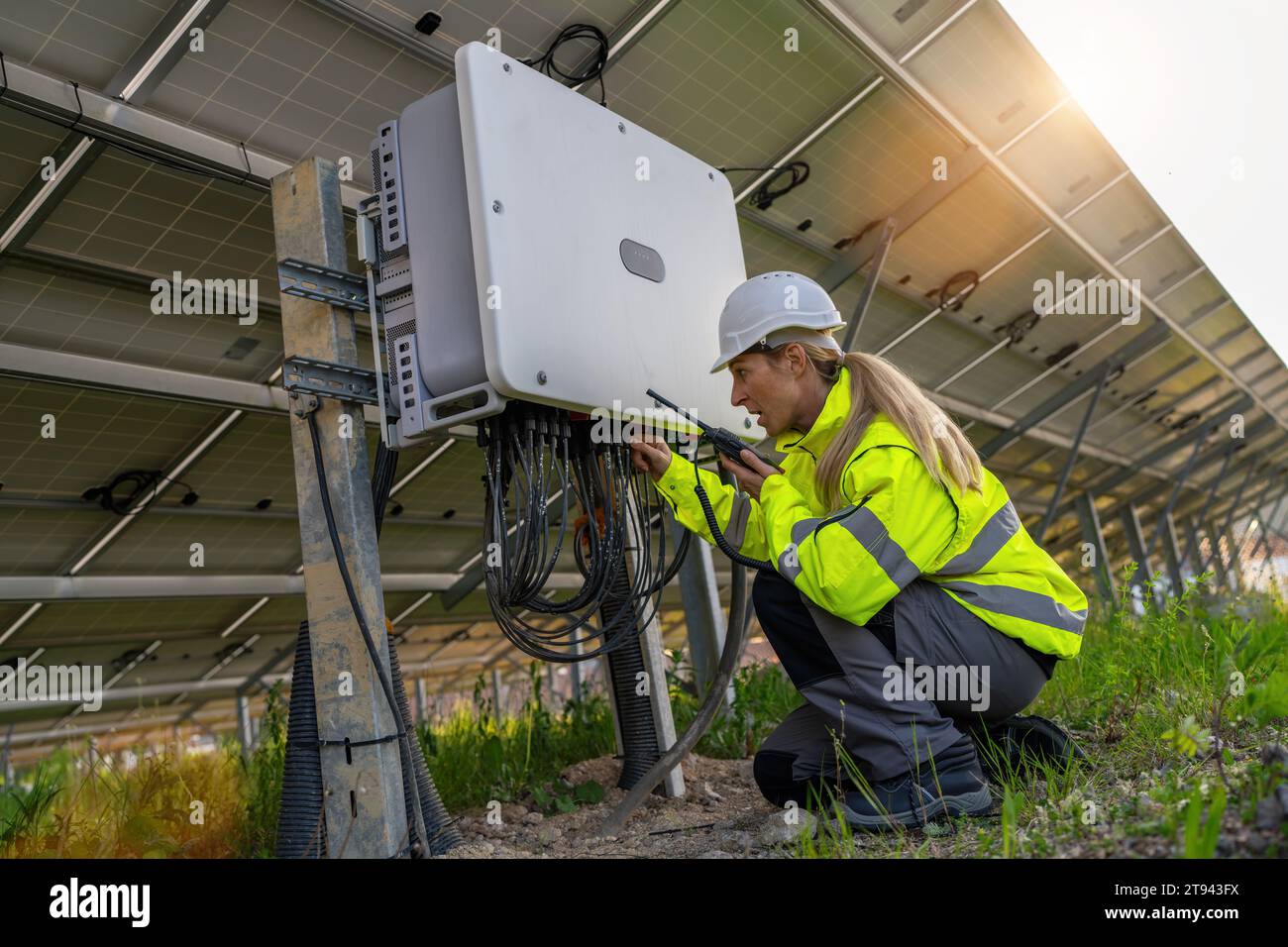 Techniker mit Walkie-Talkie, der einen Verteilerkasten an einem Solarfeld überprüft. Alternatives energetisches ökologisches Konzeptbild. Stockfoto