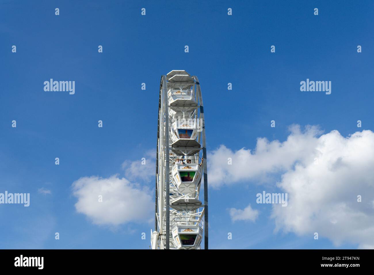 Ein vertikaler Blick auf ein Riesenrad vor dem blauen Himmel, von dem die Passagiere aus der Vogelperspektive die Umgebung genießen und Spaß haben können Stockfoto