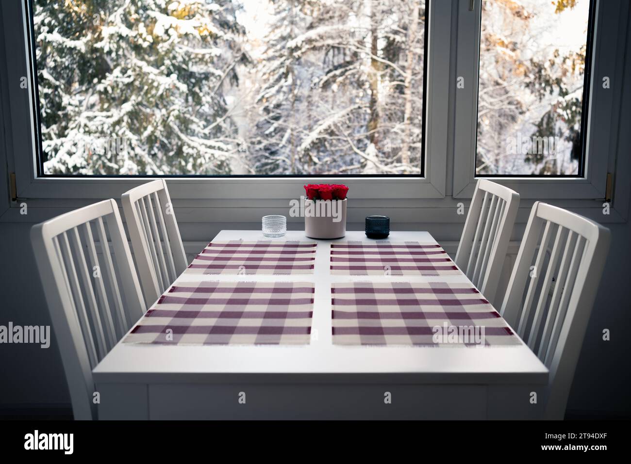 Winterfenster und Küchentisch zum Essen. Inneneinrichtung und Möbel. Schnee in Bäumen im Wald im Hintergrund. Skandinavisches Haus. Stockfoto