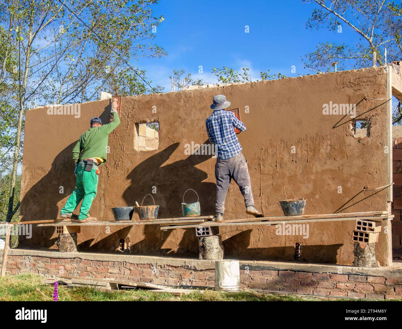 Zwei Arbeiter verputzen eine Mauer in einem sehr rustikalen und instabilen Gerüst auf einer Baustelle in der Nähe der Stadt Arcabuco im Zentrum von Colomb Stockfoto