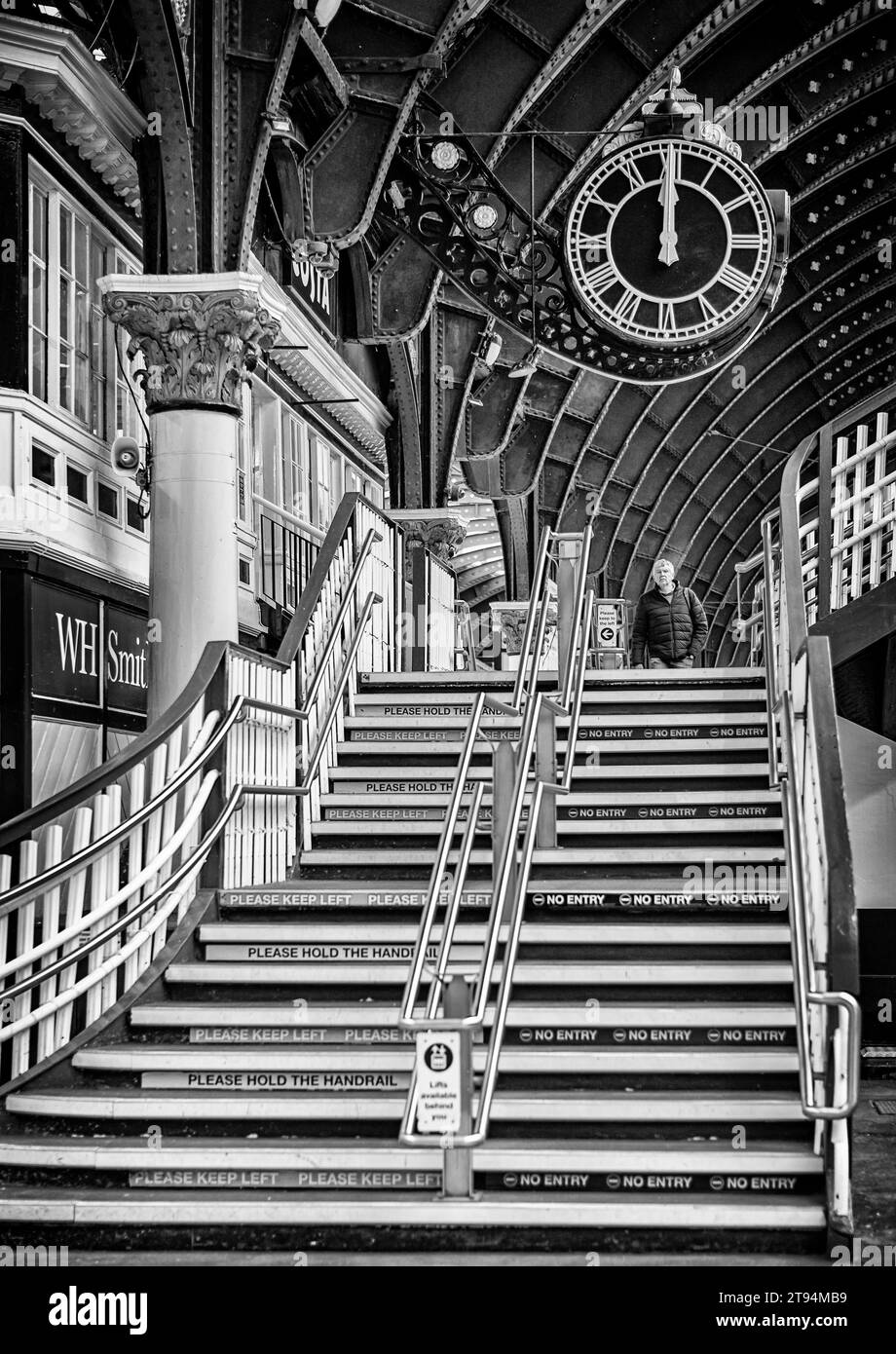 Eine Treppe in einer Bahnhofshalle führt zu einer großen kunstvollen Uhr. Eine Säule und ein Geschäft befinden sich auf einer Seite und oben ist ein historisches 19. Jahrhundert Stockfoto