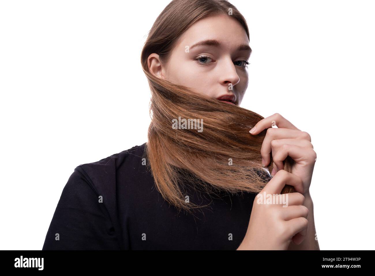 Ein hellhaariges Teenager-Mädchen in einem schwarzen T-Shirt berührt ihr seidiges Haar Stockfoto