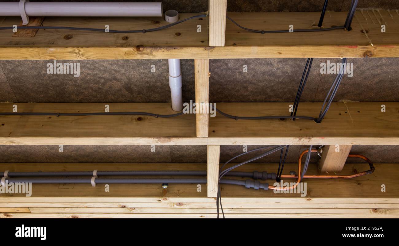 Unterbodenansicht mit verschiedenen Rohren und Kabeln in einer Holzbalkenkonstruktion mit Isoliermaterial Stockfoto
