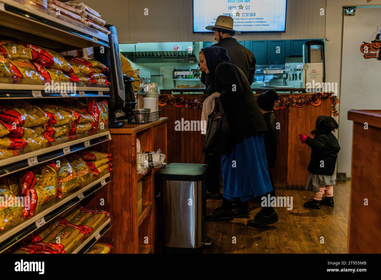 Amish-Paar mit Kindern, die auf Doud's Market, Amerikas ältestem Lebensmittelgeschäft, einkaufen. Das Geschäft wurde 1884 auf Mackinac Island eröffnet. Die traditionellen und ursprünglichen Amish sind auf Mackinac Island wegen ihrer Handwerkskunst beliebt, z. B. beim Bau und Reparieren von Wagen. Mit ihren Outfits heben sie sich kaum von Doud's Market ab, Amerikas ältestem Lebensmittelgeschäft. Mackinac Island, Michigan, Usa Stockfoto