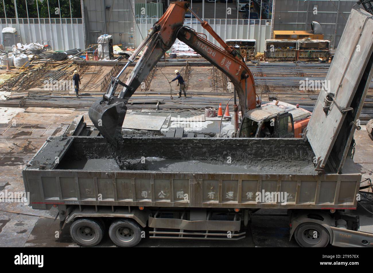 Bagger, der auf einer Baustelle während des Baus eines neuen Bürogebäudes arbeitet und einen LKW mit matschigem Boden zur Vorbereitung der Fundamentlegung beladen; Stockfoto