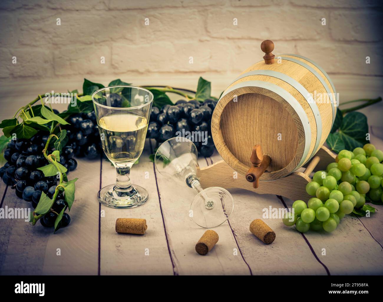 Glas Weißwein, Weinfässer, grüne und schwarze Trauben, Kork, Flaschenöffner und Efeu Stockfoto