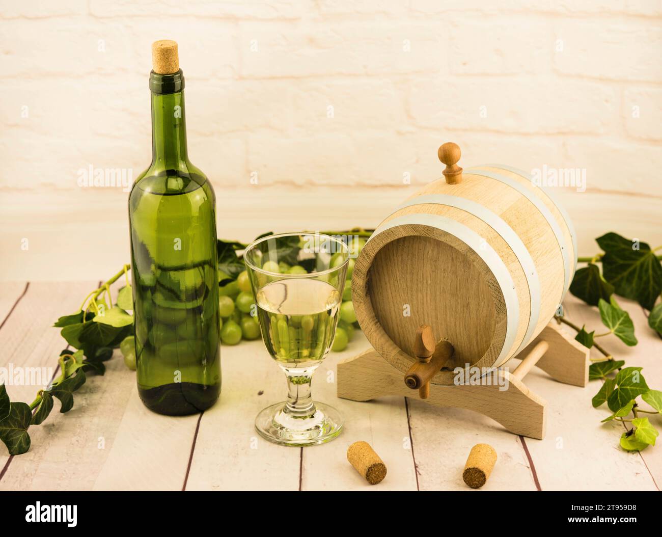 Flasche und Glas Weißwein, Weinfass, grüne Trauben, Kork, Flaschenöffner und Efeu Stockfoto