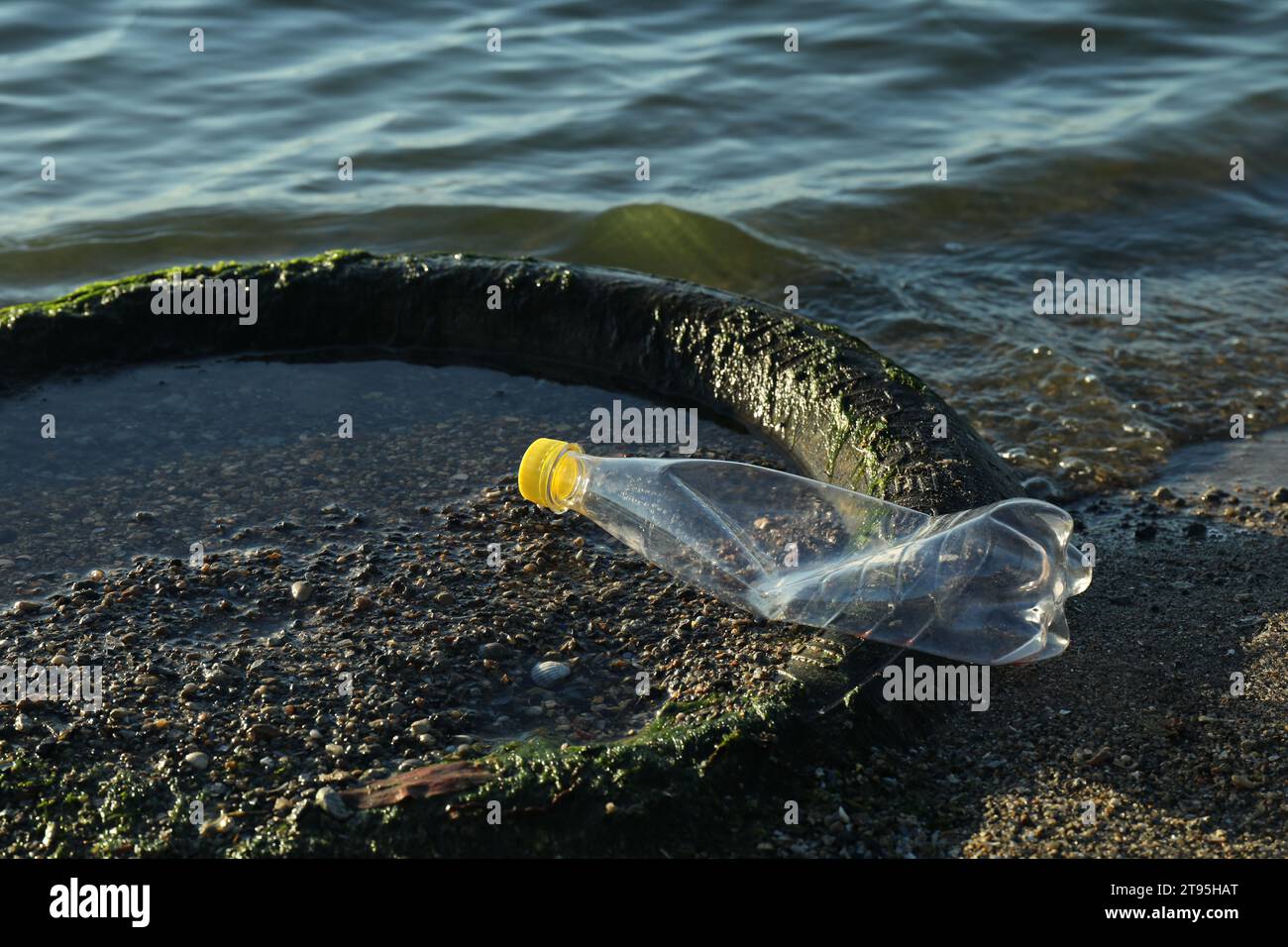 Plastikmüll und Reifen auf Sand in der Nähe von Wasser. Umweltverschmutzung Stockfoto