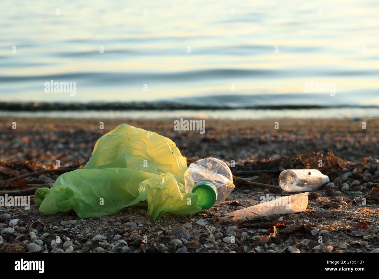 Plastikbeutel und Flaschen auf Sand in der Nähe von Wasser. Umweltverschmutzung Stockfoto