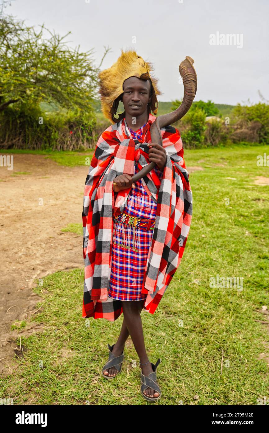 Maasai Mara, Kenia, 25. Dezember 2020 - Ein junger Maasai-Häuptling und Krieger, der ein traditionelles shuka-Kleid mit einem Löwenhautkopf-Kleid und einem Kudu-Horn trägt Stockfoto