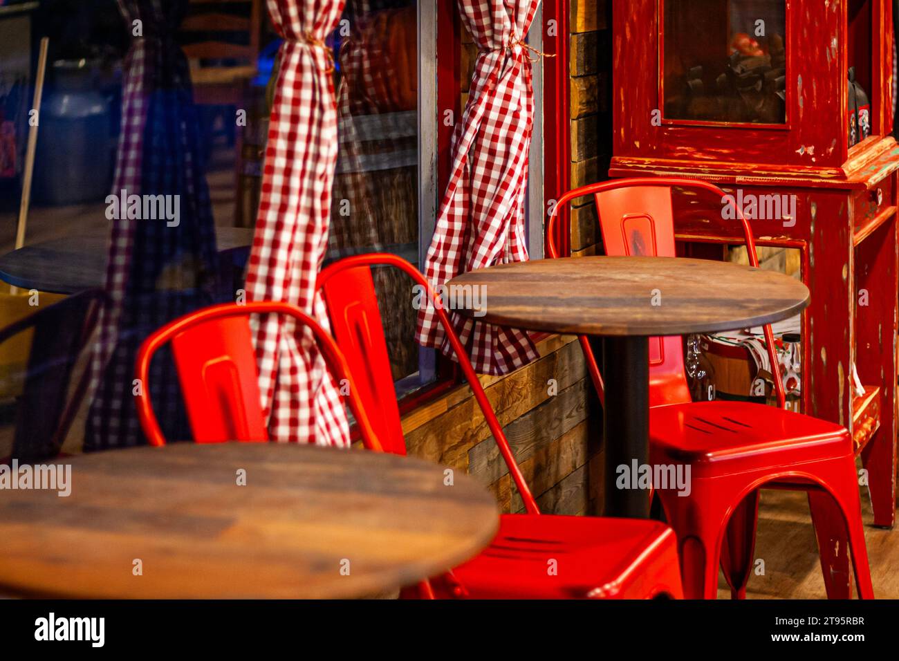 Rote Stühle an Holztischen in einem Geschäft mit roten und weißen Gingham-Vorhängen an den Fenstern Stockfoto