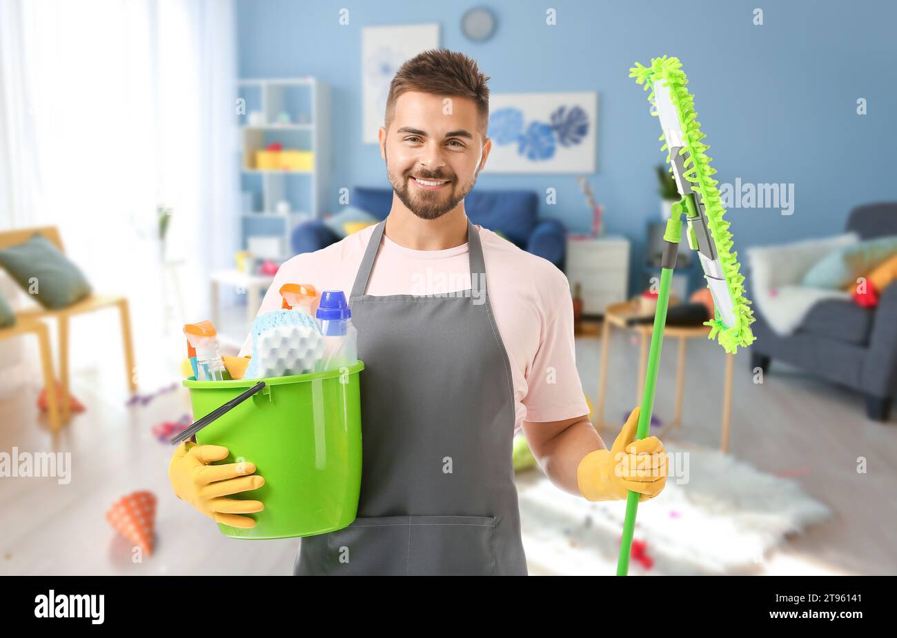 Männlicher Hausmeister mit Putzmitteln in einem unordentlichen Raum nach der Party Stockfoto