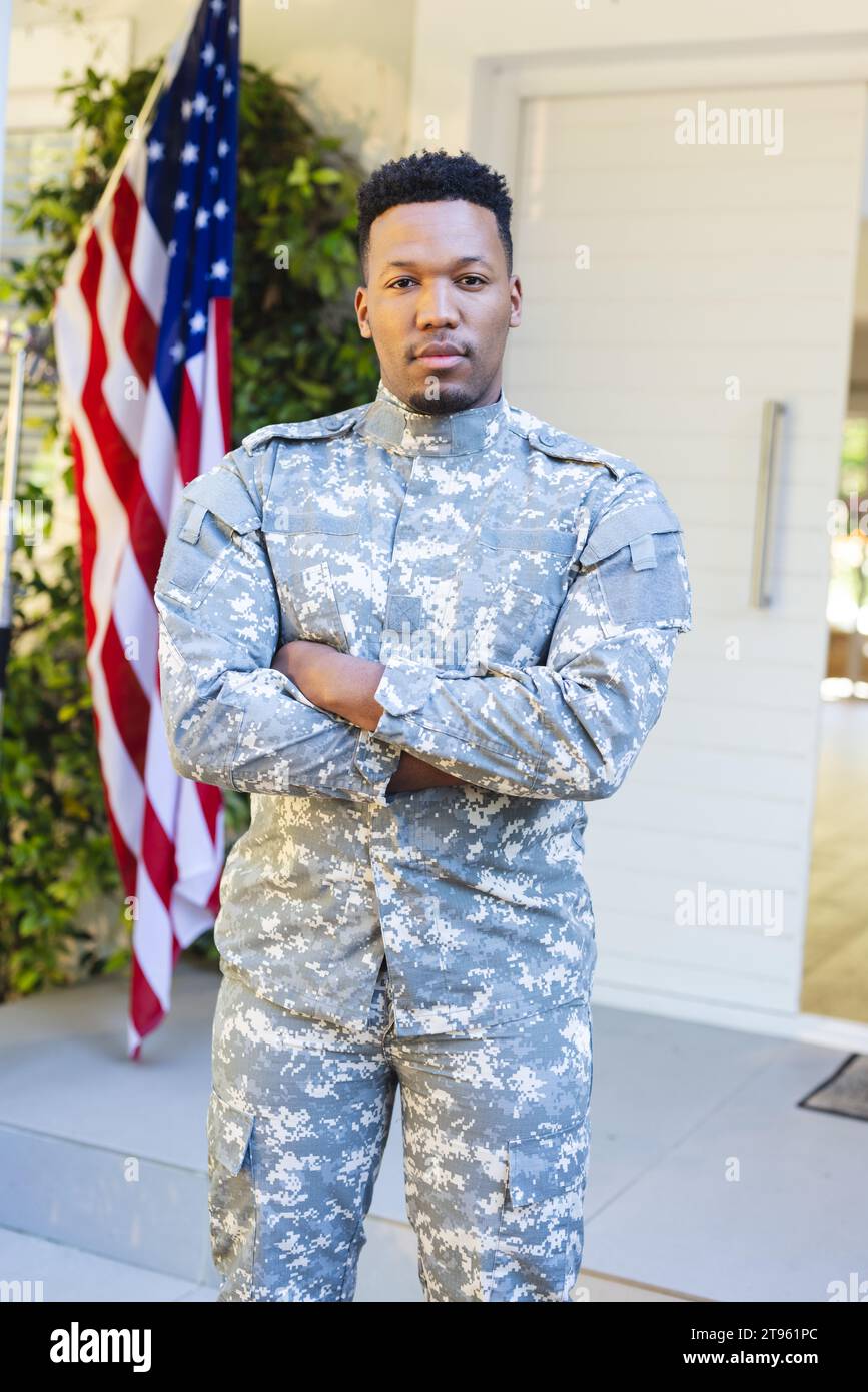 Männlicher afroamerikanischer Soldat, der mit Armen vor dem Haus steht, mit us-Flagge, Kopierraum Stockfoto