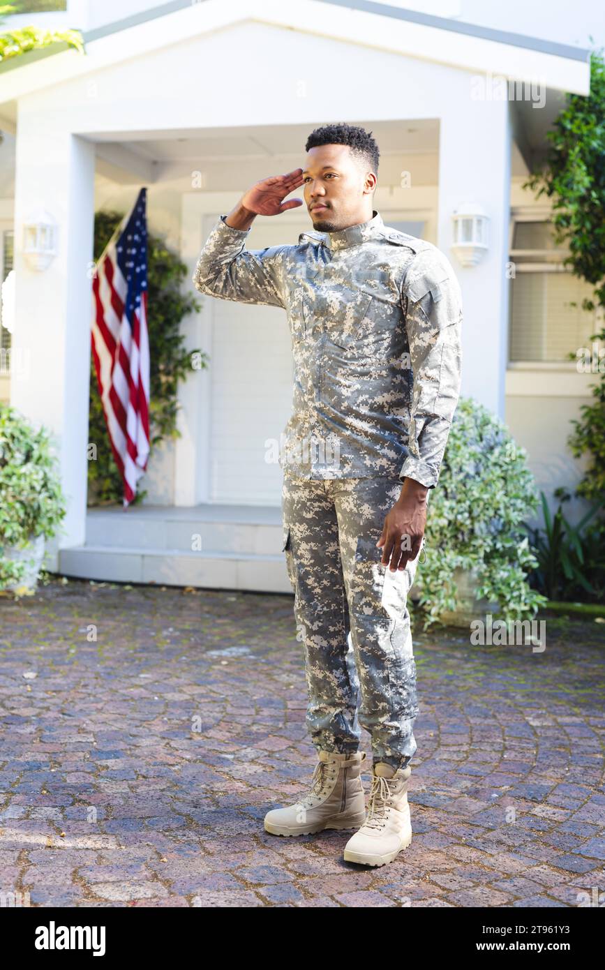 Fokussierter afroamerikanischer männlicher Soldat, der vor dem Haus steht und mit us-Flagge grüßt, Kopierraum Stockfoto