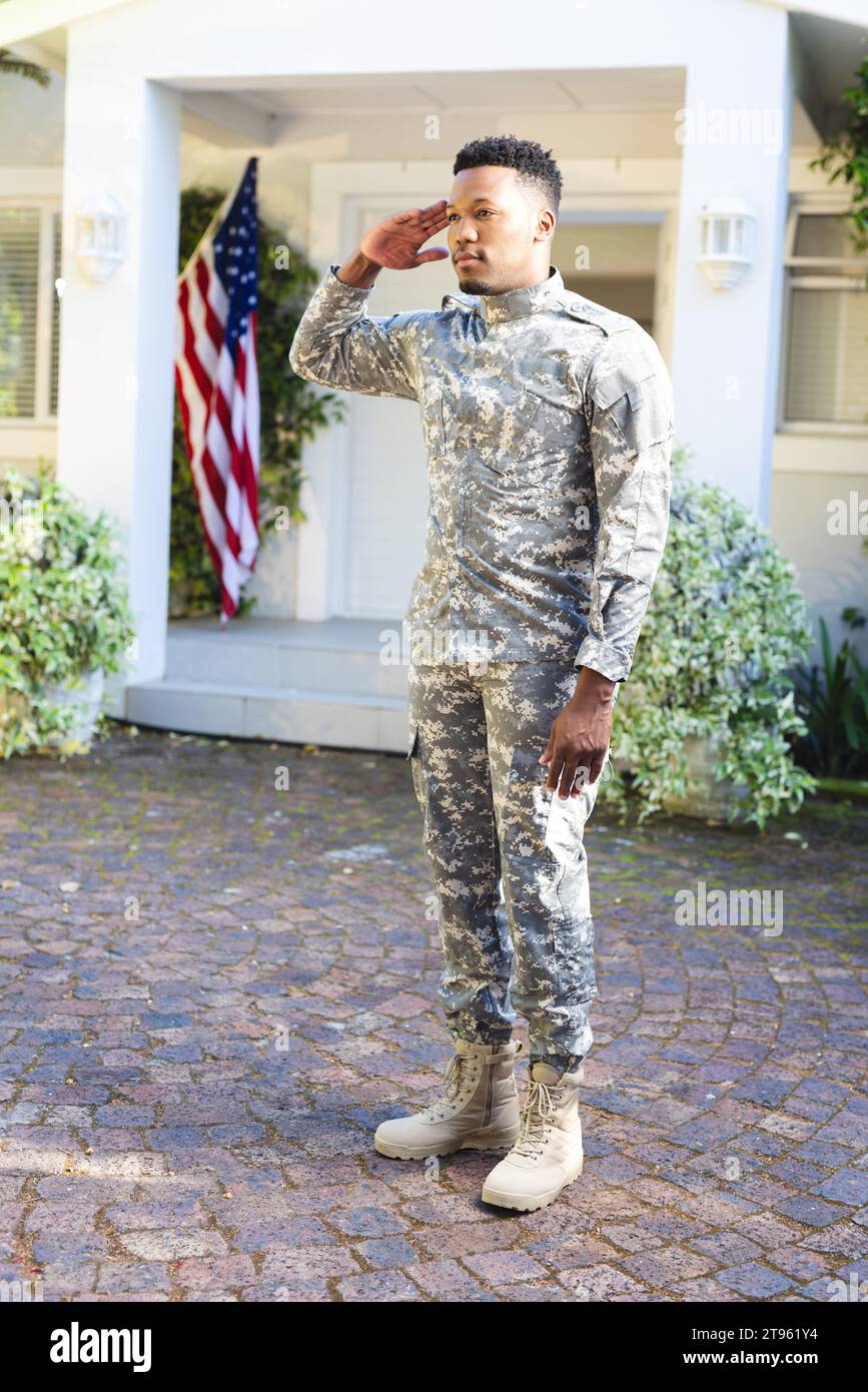 Fokussierter afroamerikanischer männlicher Soldat, der vor dem Haus steht und mit us-Flagge grüßt, Kopierraum Stockfoto