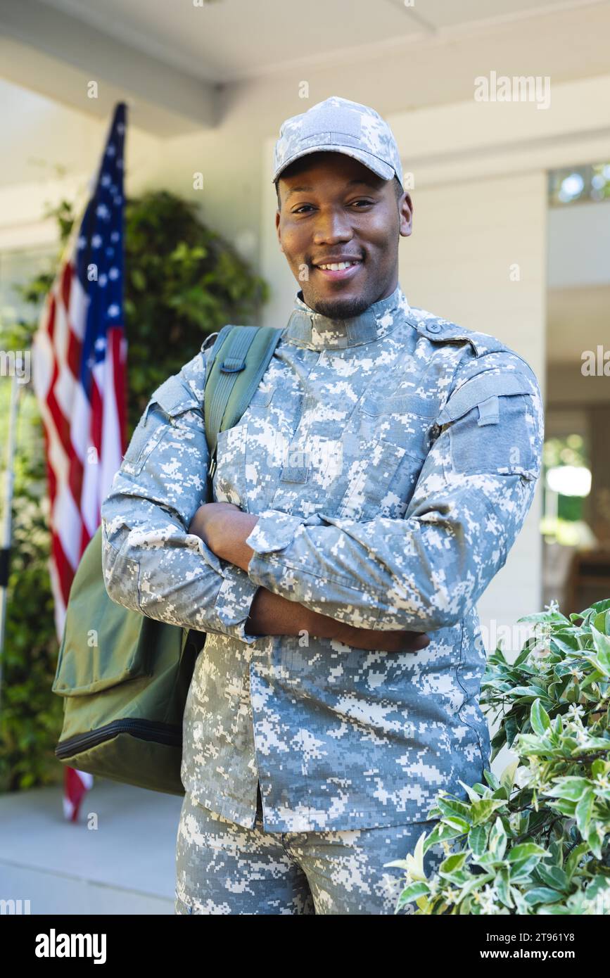 Glücklicher afroamerikanischer Soldat mit gekreuzten Armen vor dem Haus mit us-Flagge, Kopierraum Stockfoto