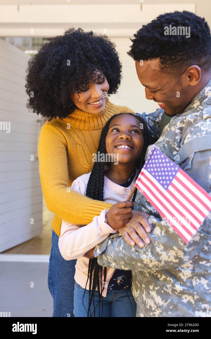 Glücklicher afroamerikanischer Soldat, der seine Familie vor dem Haus umschließt, mit us-Flagge, Kopierraum Stockfoto