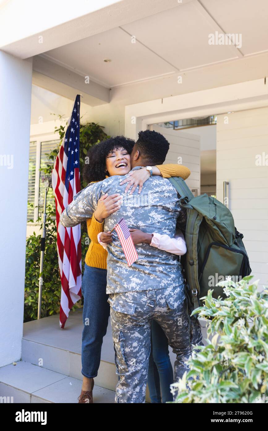 Glücklicher afroamerikanischer Soldat, der seine Familie vor dem Haus umschließt, mit us-Flagge, Kopierraum Stockfoto