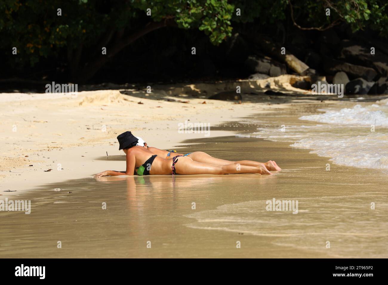 Frauen in Bikinis sonnen sich an einem Sandstrand auf felsigem Hintergrund. Konzept der Entspannung und genießen der Sonne, Urlaub an der tropischen Küste Stockfoto