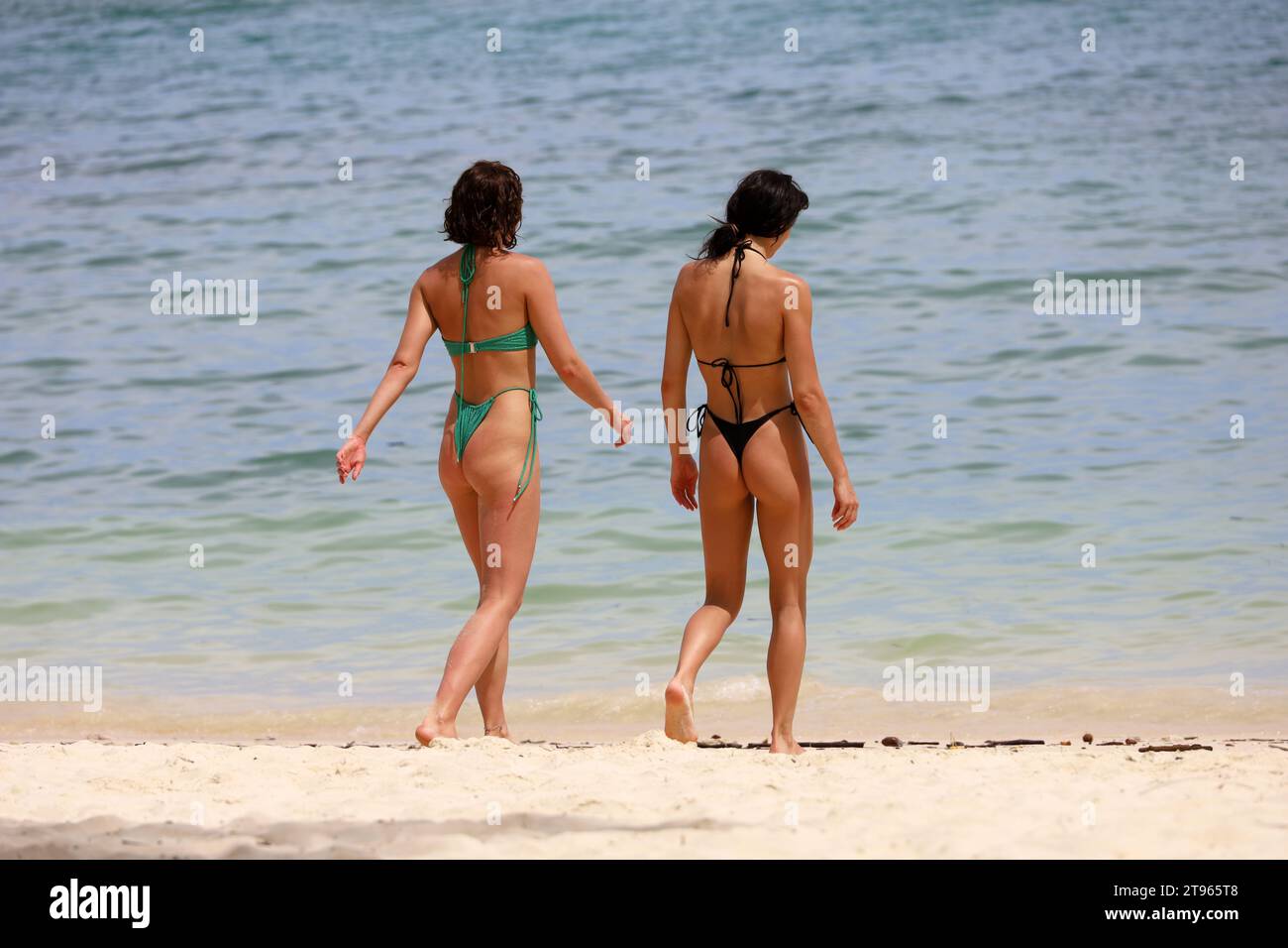 Zwei schlanke Mädchen im Bikini, die am tropischen Strand am Sand spazieren. Seeküste, Freundinnen im Ferienort Stockfoto
