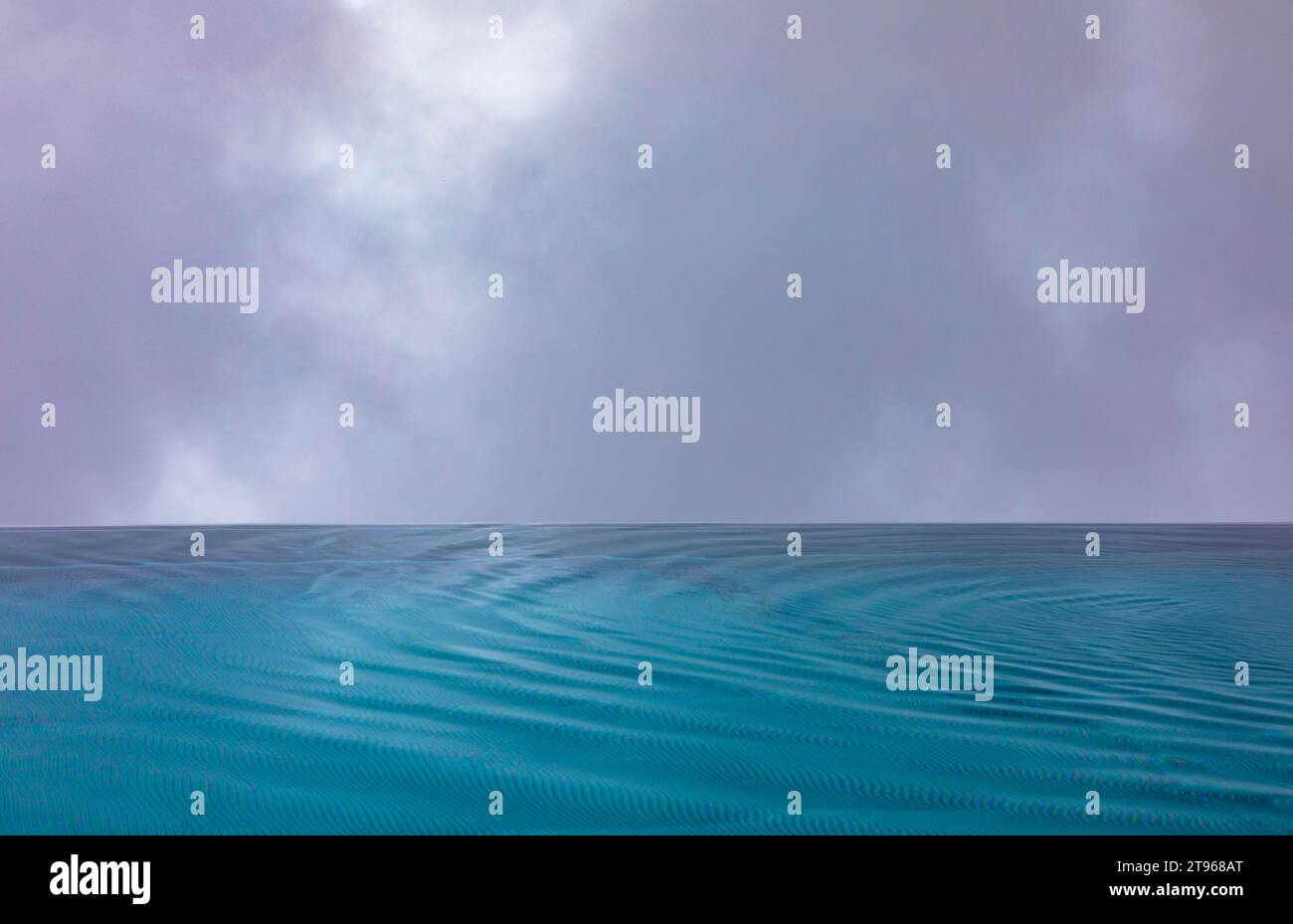 Gewellte Wasseroberfläche bei Regen im Schwimmbad mit dramatischem bewölktem Himmel, Österreich Stockfoto