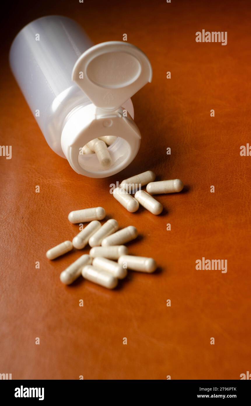 Pillen, die aus der Pillenflasche auf braunem Lederhintergrund verschüttet werden. Fokus auf den Vordergrund. Stockfoto
