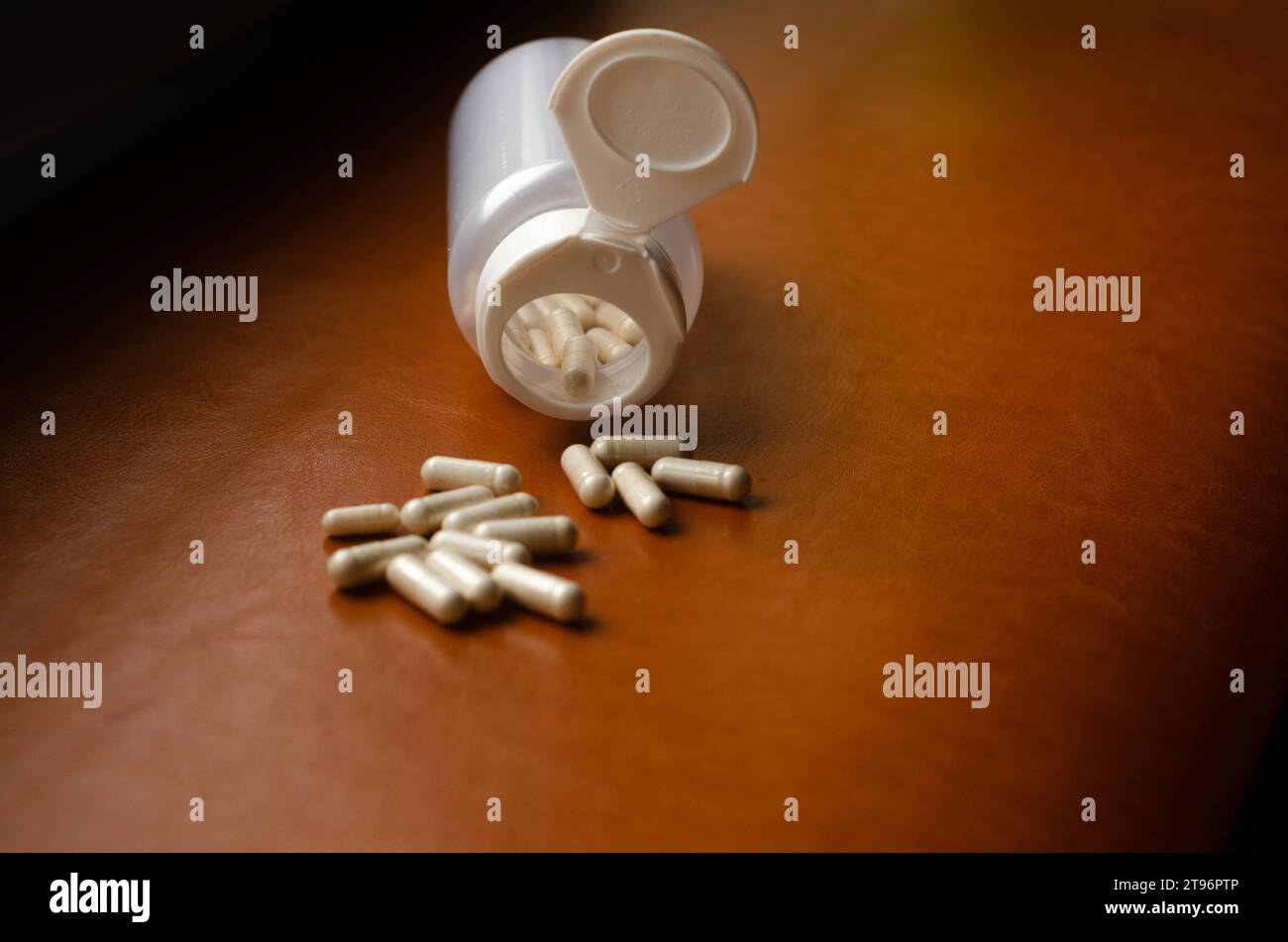 Pillen, die aus der Pillenflasche auf braunem Lederhintergrund verschüttet werden. Fokus auf den Vordergrund. Stockfoto