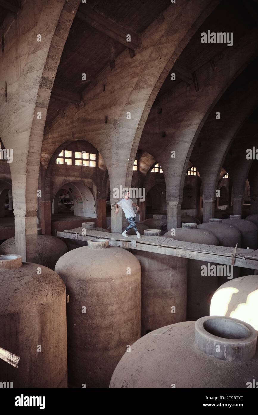 Entfernter Mann tanzt auf Betonüberführung gegen große Fässer in vergessener Grunge-Kathedrale mit Bogengängen Stockfoto