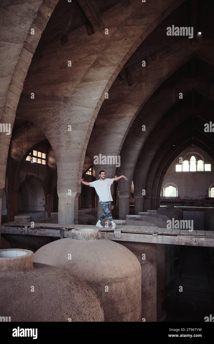 Tänzerin mit gespreizten Armen, die auf Überführungen vor bogenförmigen Passagen in einer alten, staubigen Kathedrale mit großen Fässern einen Break-Tanz vorführen Stockfoto