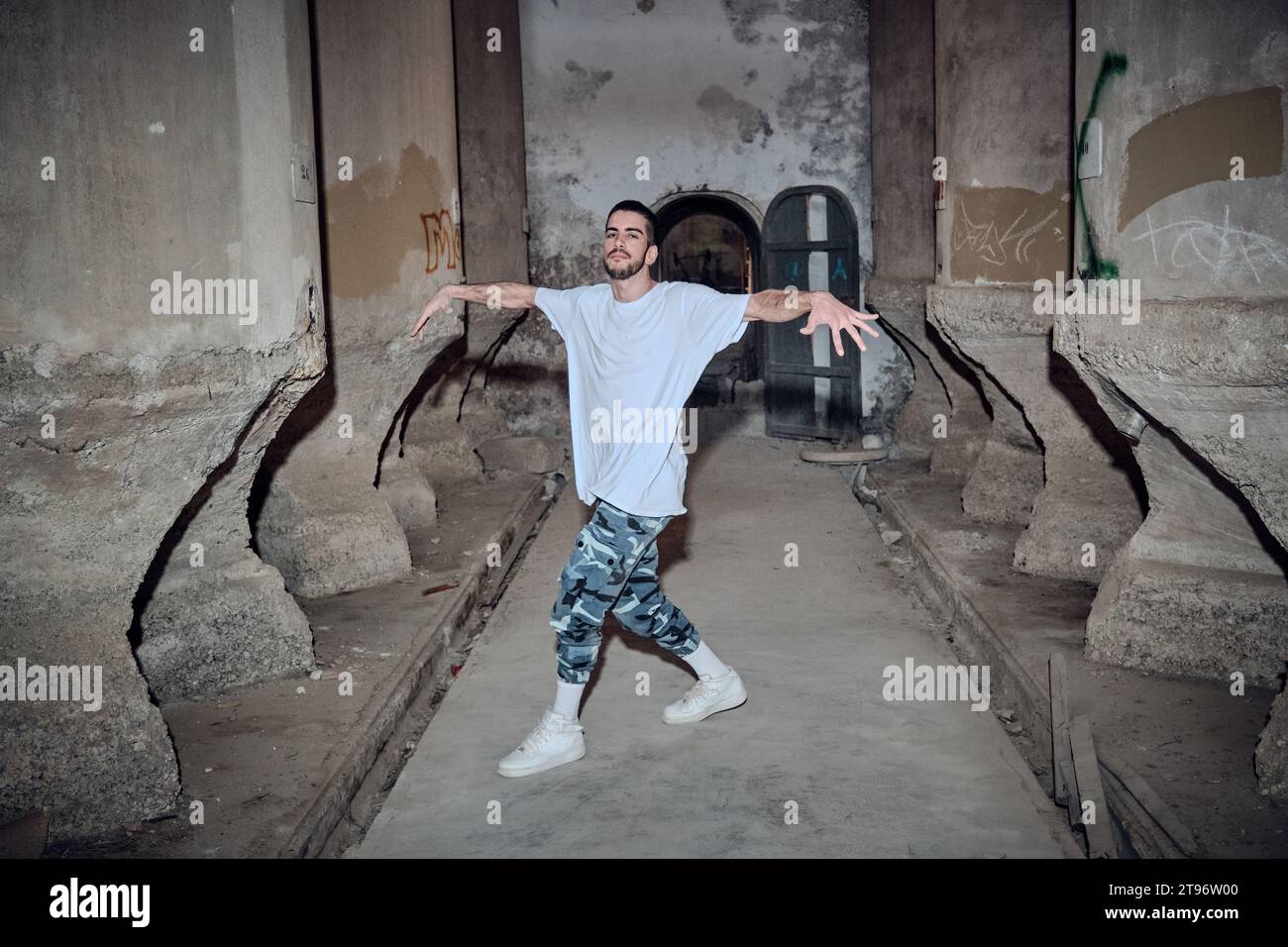 Ein ganzer Körper erfahrener Männer in Freizeitkleidung, der in die Kamera blickt, während er Breakdance-Bewegungen in einem alten verlassenen Gebäude vorführt Stockfoto