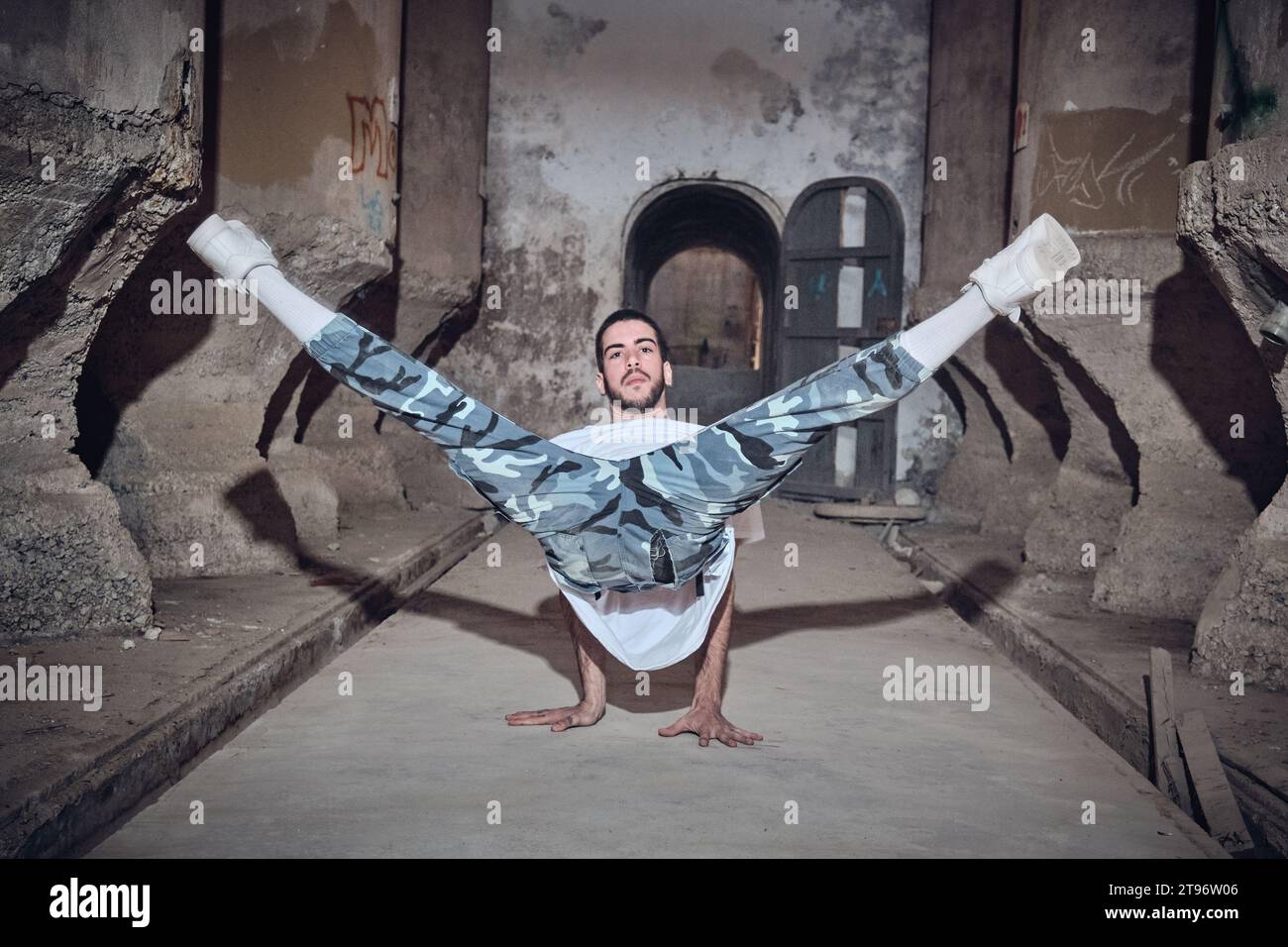 Voller Körper talentierter Männer in Freizeitkleidung, die in die Kamera blicken, während sie in einem alten verlassenen Gebäude mit schäbigen Wänden tanzen Stockfoto