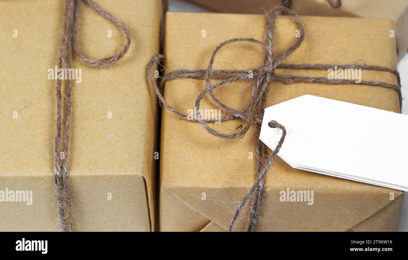 Leere Papierkarte auf handgefertigten braunen Geschenkkartons, die in handgefertigtes Papier gewickelt sind. Postkartenvorlage für Weihnachtsgrüße Stockfoto