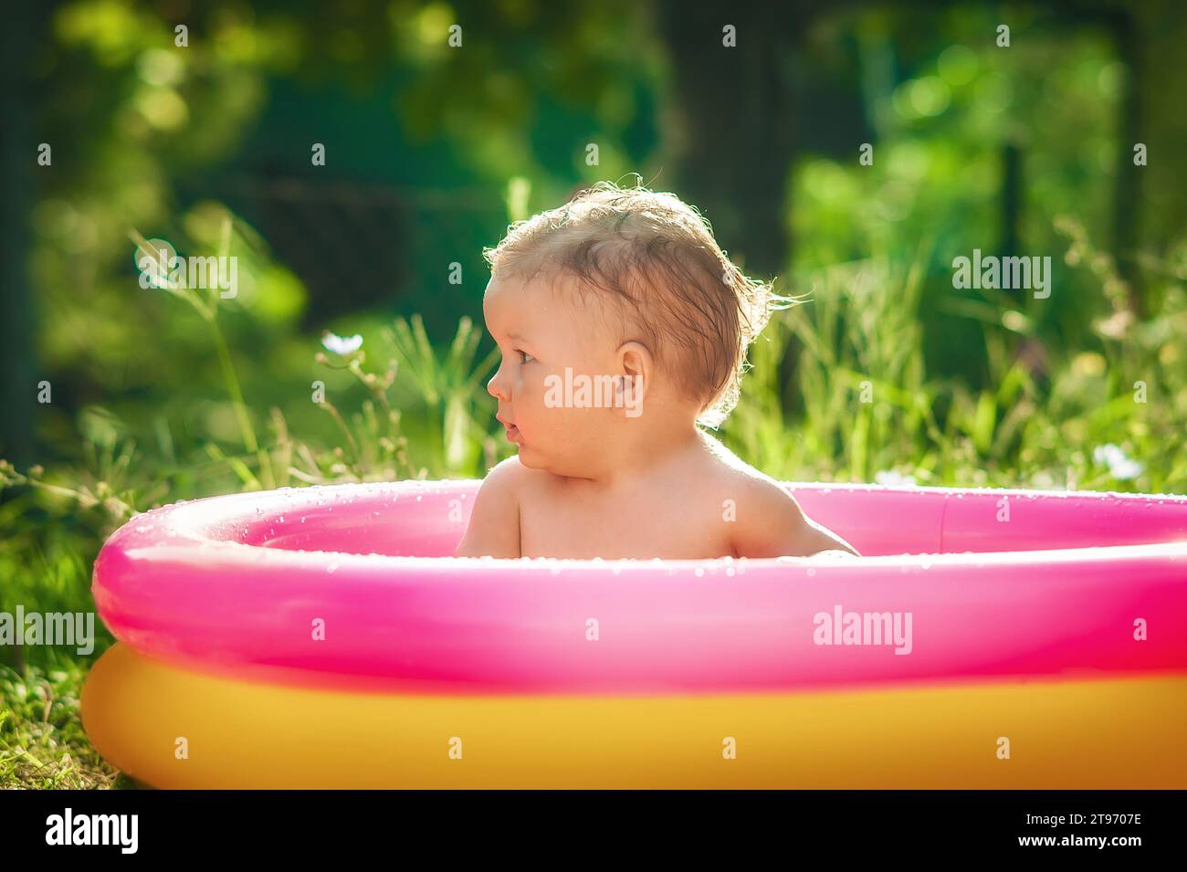Kleiner Junge, der in einem Pool im Garten sitzt. Heißer Sommertag in der Natur Stockfoto