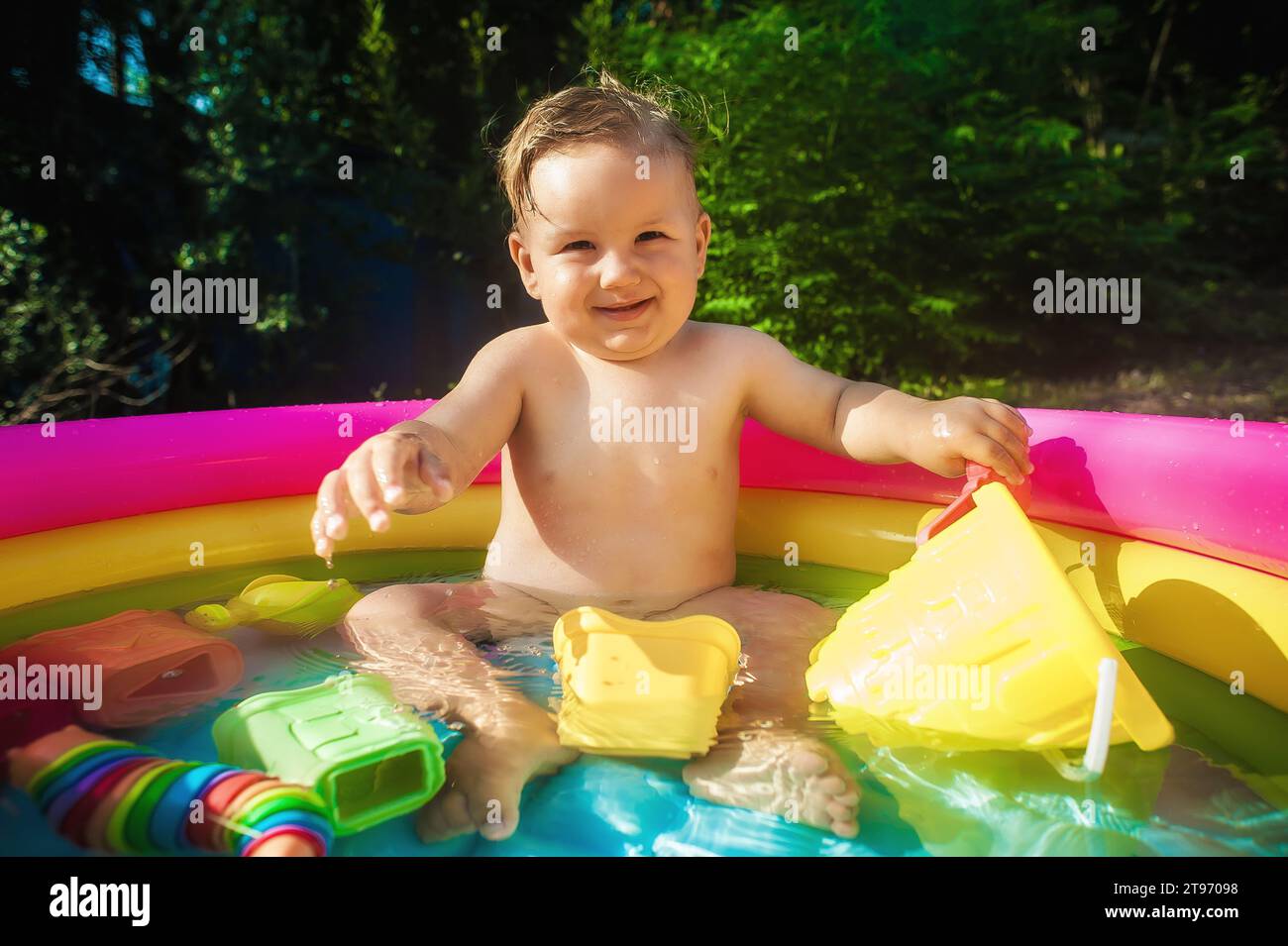 Junge, der in einem Pool im Garten sitzt und mit Wasserspielzeug spielt. Heißer Sommertag in der Natur Stockfoto