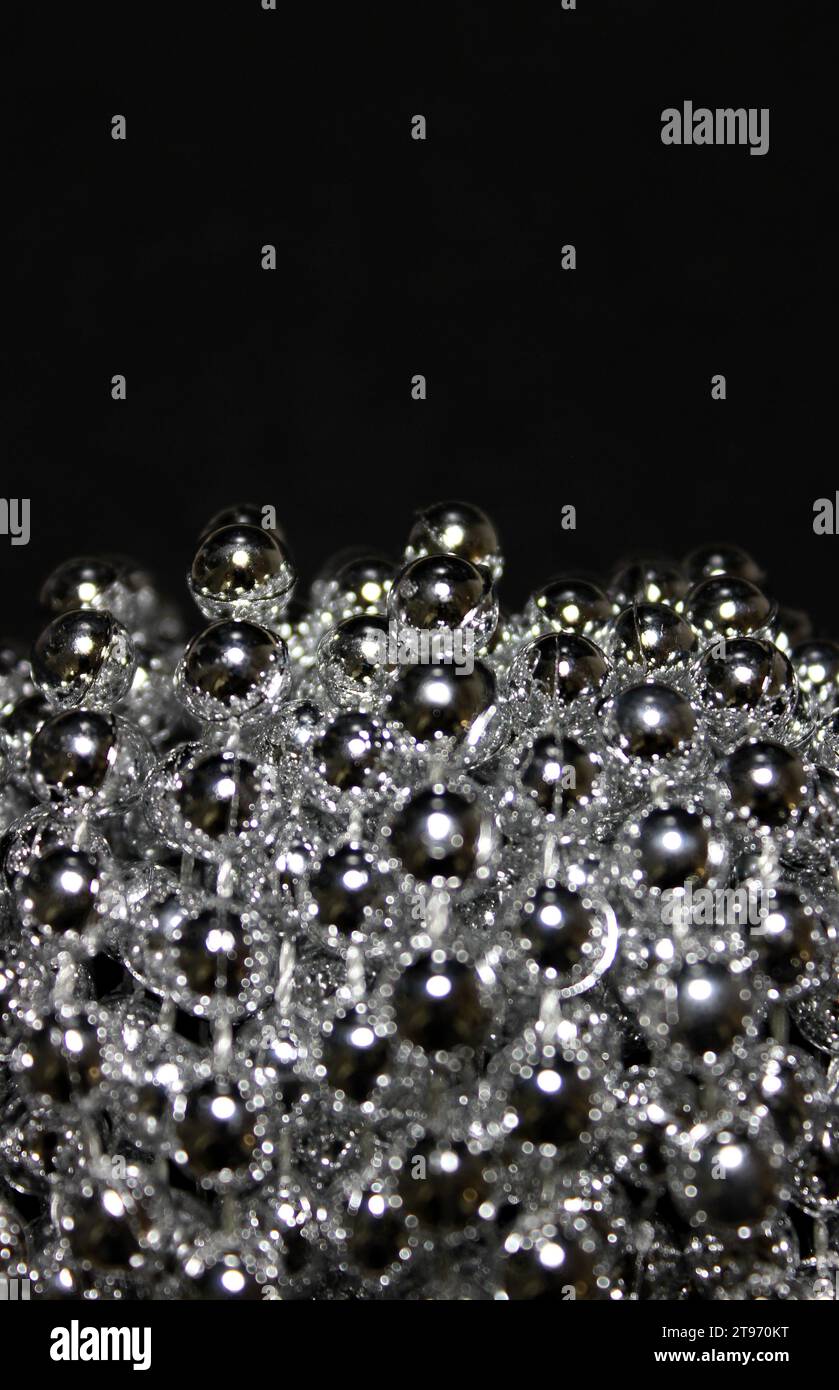 Vertikales Foto von kleinen glitzernden Perlen in Einem Bündel über schwarzem Hintergrund Stockfoto