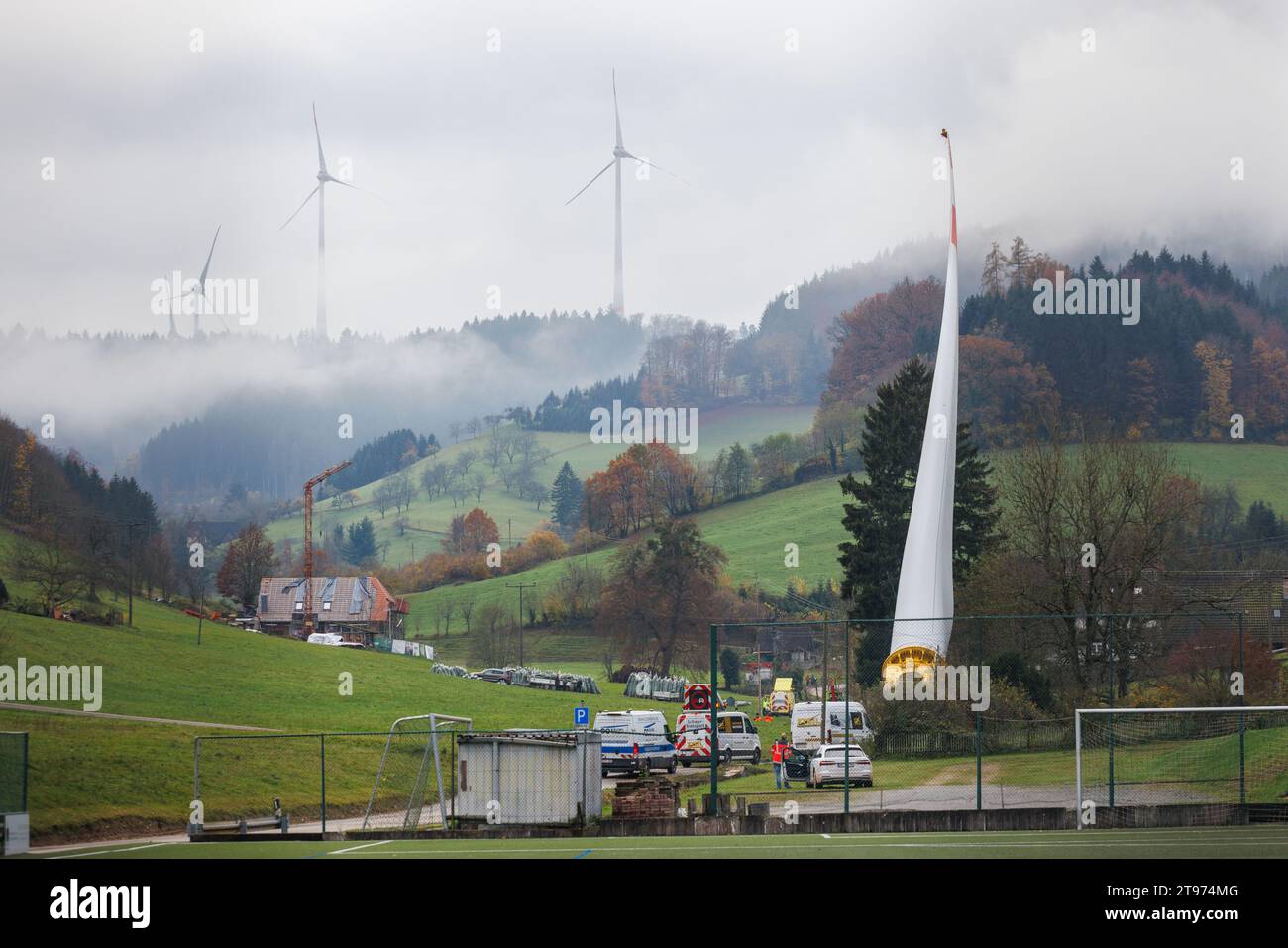 23. November 2023, Baden-Württemberg, Biberach: Auf einem sogenannten selbstfahrenden Transporter wird ein Windenergieschaufel montiert und durch das Dorf Prinzbach transportiert, während andere Windenergieanlagen im Hintergrund zu sehen sind. Insgesamt sollen drei 68 Meter lange Rotorblätter aus Biberach über eine Entfernung von rund sieben Kilometern transportiert werden. Nach Angaben des Energieversorgers Badenova sind millimetergenaue Arbeiten erforderlich, um sicherzustellen, dass die Rotorblätter die Baustelle unbeschädigt erreichen. An einigen Stellen entlang der Strecke muss eine Steigung von 12 Prozent gemeistert werden. Foto: Philipp Stockfoto