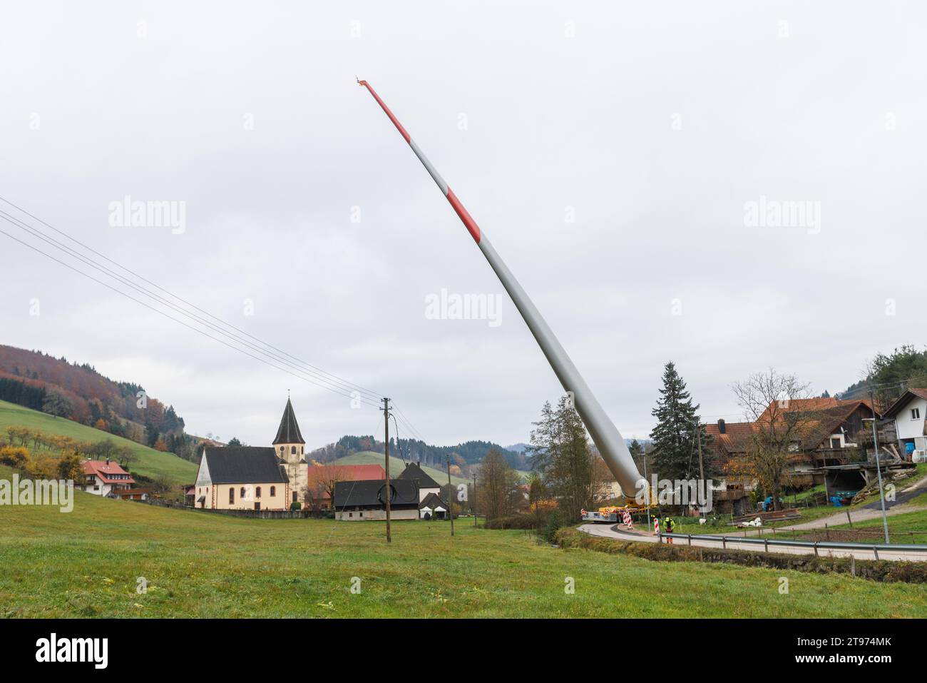 Biberach, Deutschland. November 2023. Auf einem sogenannten selbstfahrenden Transporter wird ein Windenergieblatt montiert und durch das Dorf Prinzbach transportiert. Insgesamt sollen drei 68 Meter lange Rotorblätter aus Biberach über eine Entfernung von rund sieben Kilometern transportiert werden. Nach Angaben des Energieversorgers Badenova sind millimetergenaue Arbeiten erforderlich, um sicherzustellen, dass die Rotorblätter unbeschädigt auf der Baustelle ankommen. An einigen Stellen entlang der Strecke muss eine Steigung von 12 Prozent gemeistert werden. Quelle: Philipp von Ditfurth/dpa/Alamy Live News Stockfoto