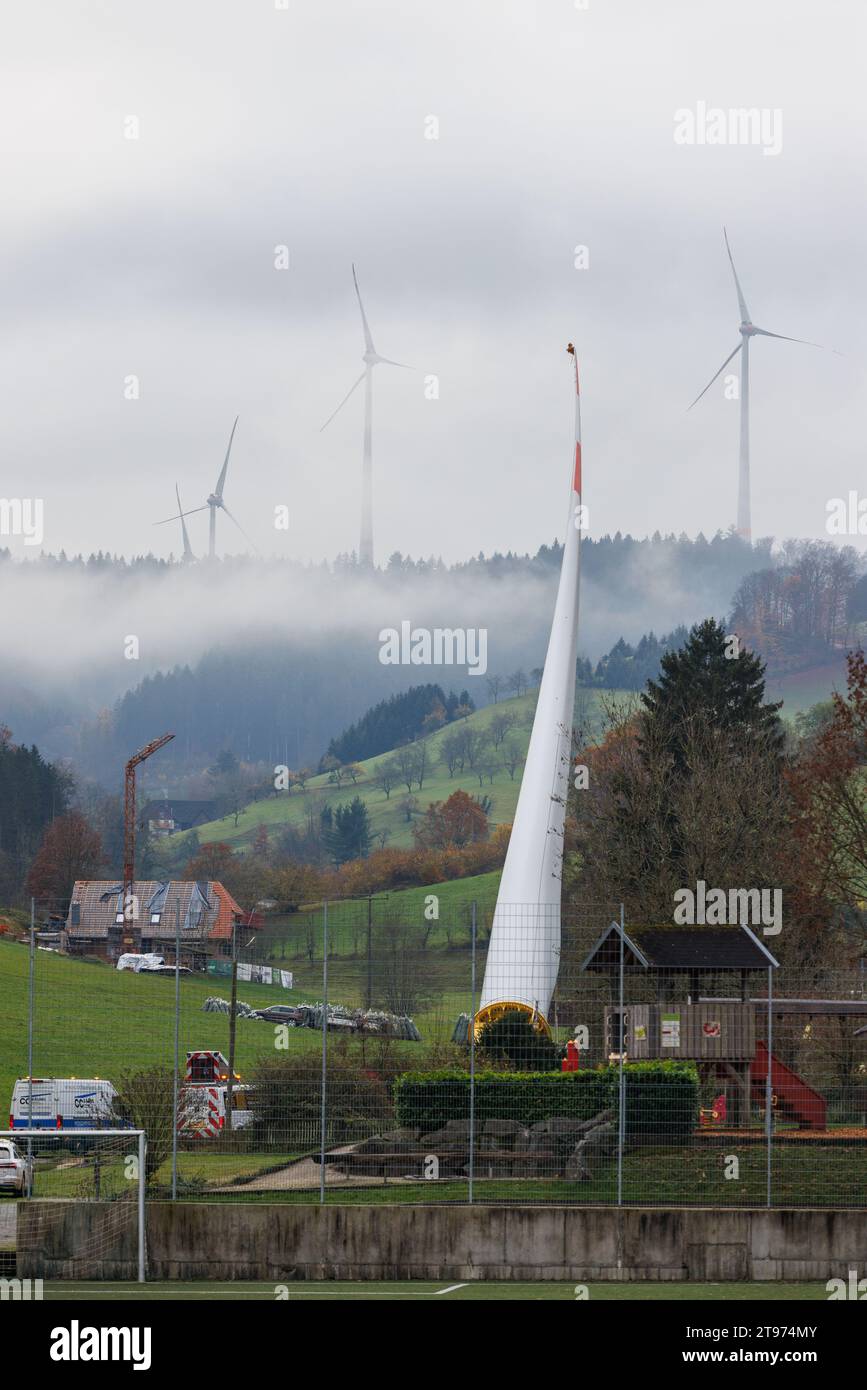 23. November 2023, Baden-Württemberg, Biberach: Auf einem sogenannten selbstfahrenden Transporter wird ein Windenergieschaufel montiert und durch das Dorf Prinzbach transportiert, während andere Windenergieanlagen im Hintergrund zu sehen sind. Insgesamt sollen drei 68 Meter lange Rotorblätter aus Biberach über eine Entfernung von rund sieben Kilometern transportiert werden. Nach Angaben des Energieversorgers Badenova sind millimetergenaue Arbeiten erforderlich, um sicherzustellen, dass die Rotorblätter die Baustelle unbeschädigt erreichen. An einigen Stellen entlang der Strecke muss eine Steigung von 12 Prozent gemeistert werden. Foto: Philipp Stockfoto