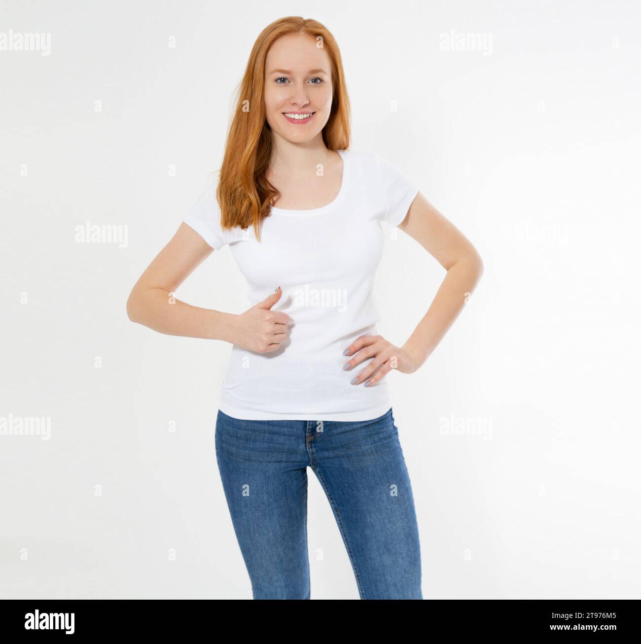 Wunderschönes Mädchen mit rotem Haar zeigt ein Schild auf einem weißen T-Shirt isoliert. Hübsches Lächeln, rothaarige Frau im T-Shirt, leer. Stockfoto