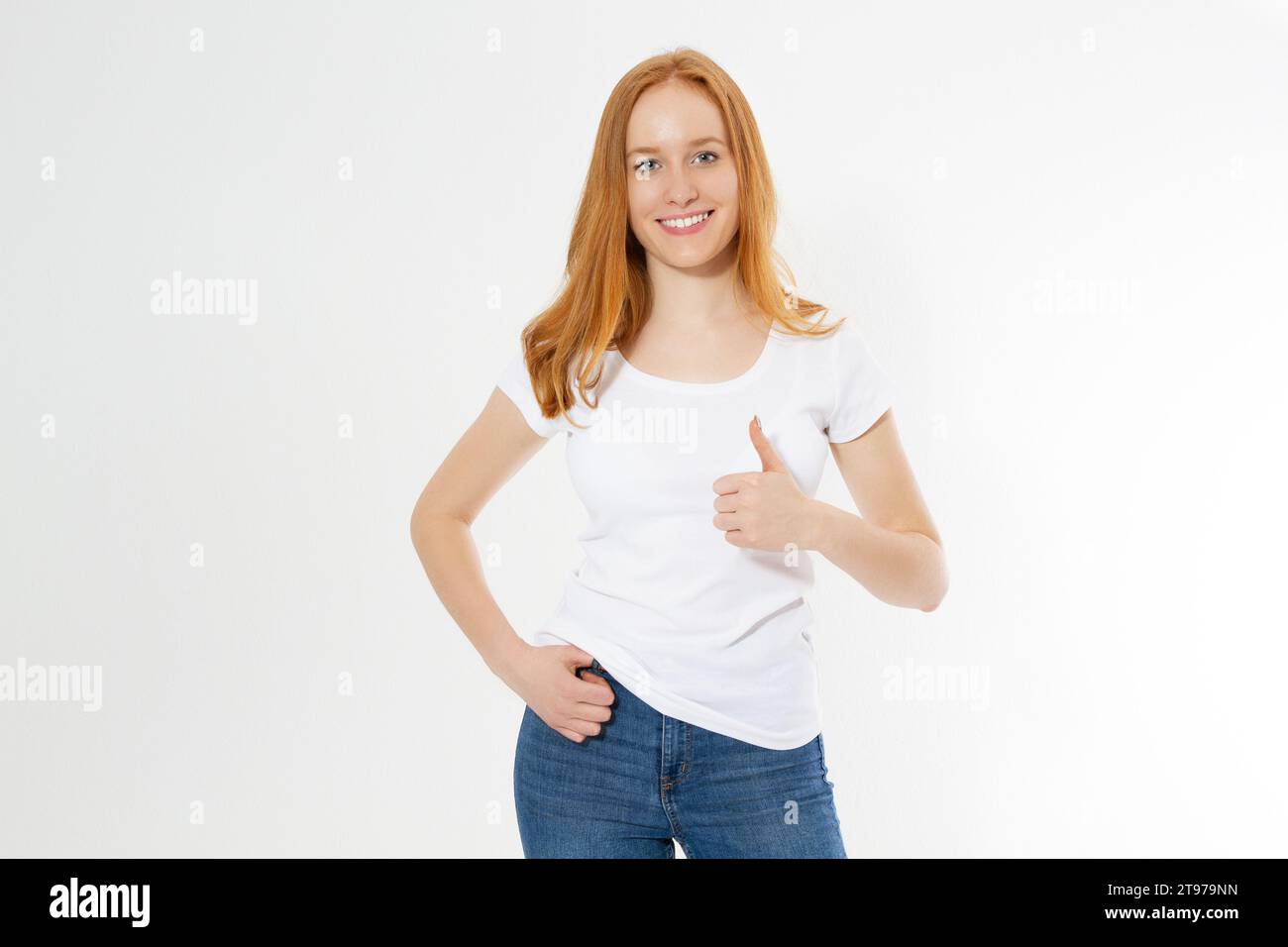 Wunderschönes Mädchen mit rotem Haar zeigt ein Schild auf einem weißen T-Shirt isoliert. Hübsches Lächeln, rothaarige Frau im T-Shirt, leer. Stockfoto