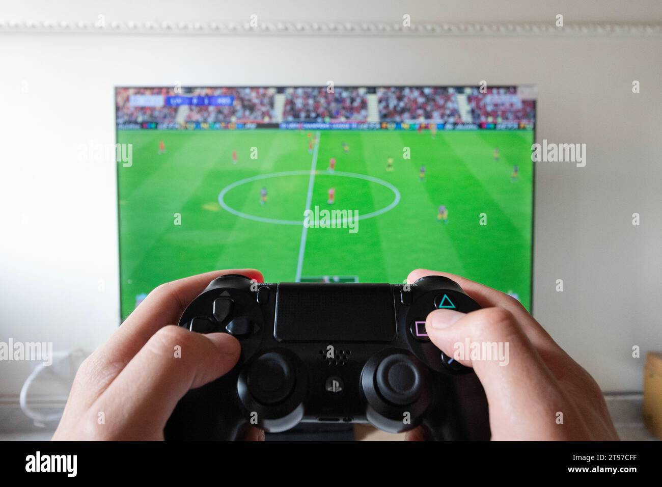 Eine männliche Hand, die einen Controller für die Spielstation 4 mit einem Fußballvideospiel in einem Smart-tv im Hintergrund hält Stockfoto
