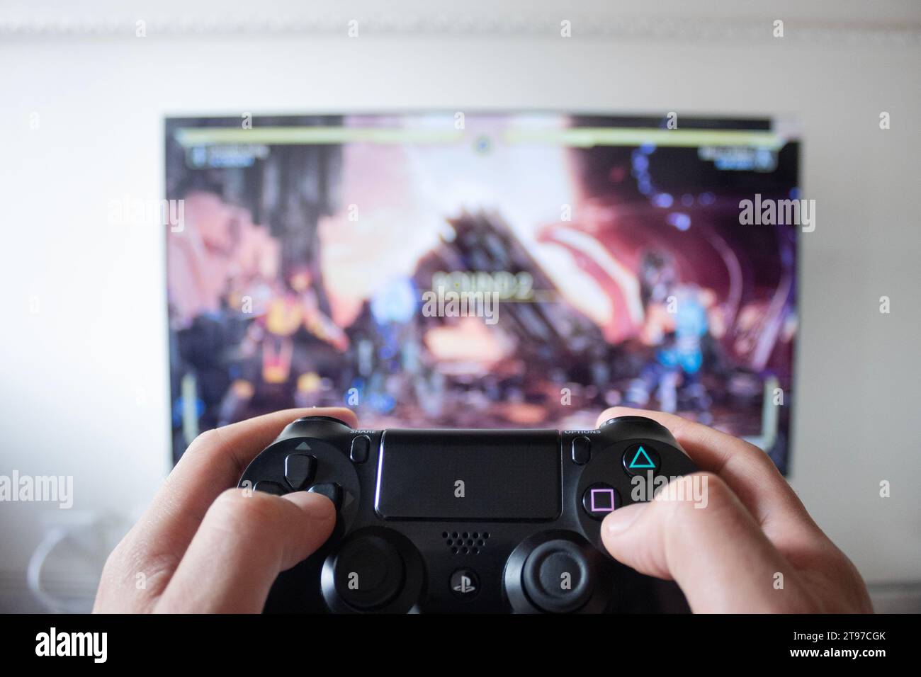 Eine männliche Hand, die einen Controller für die Spielstation 4 mit einem Kampfflugzeug-Videospiel in einem Smart-tv im Hintergrund hält Stockfoto