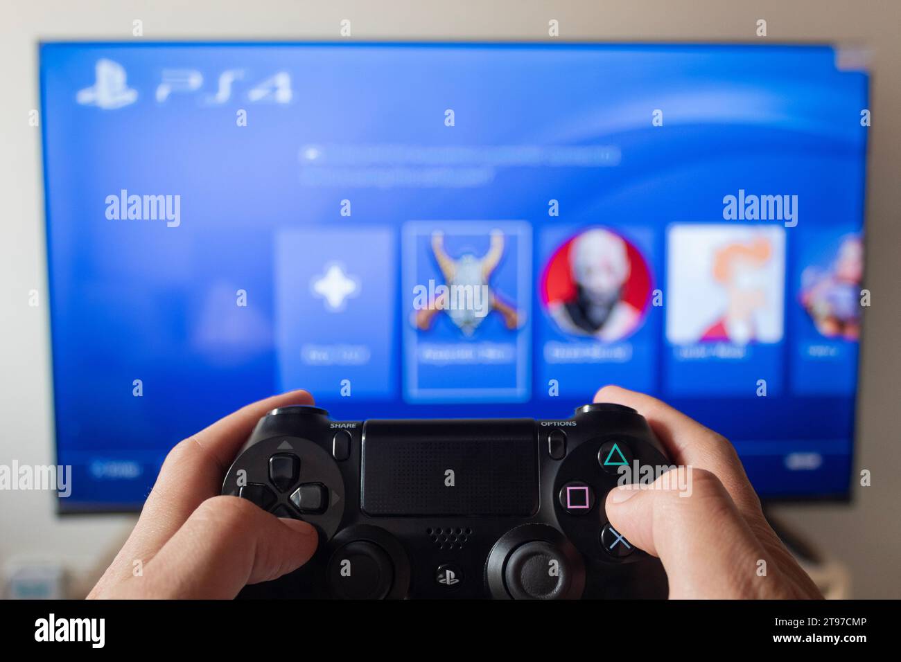 Eine männliche Hand, die einen Controller für Play Station 4 mit Schnittstelle für Play Station 4 in einem Smart-tv im Hintergrund hält Stockfoto
