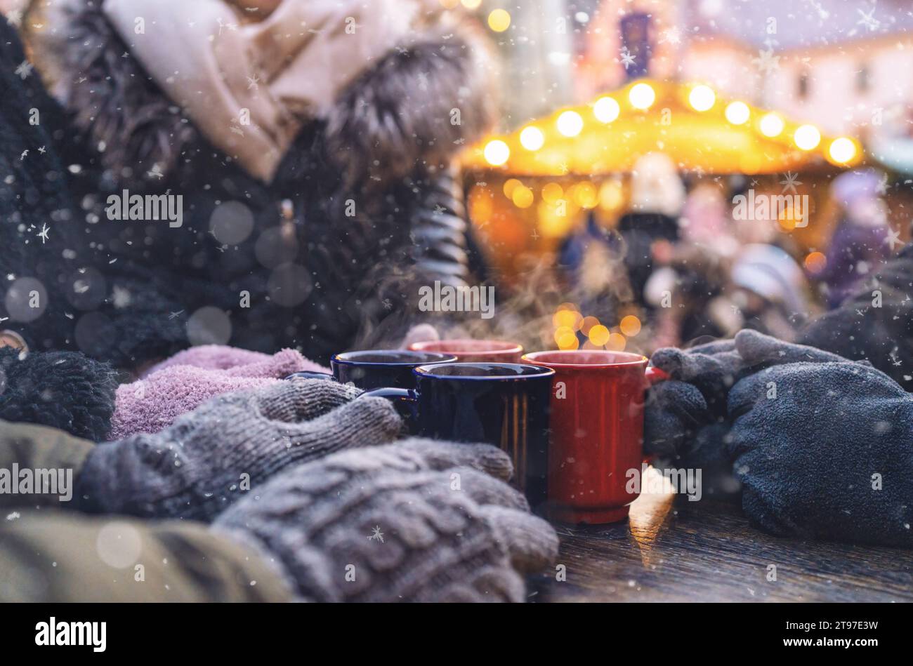 Hände in Handschuhen um dampfende Tassen mit Glühwein auf einem weihnachtsmarkt, mit Copyspace für Ihren individuellen Text. Stockfoto