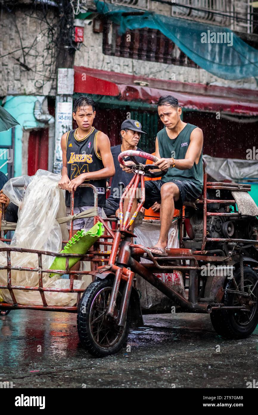Einige philippinische Arbeiter liefern in den geschäftigen Straßen von Manila, den Philippinen, Waren mit einem Lkw im Traktorstil. Stockfoto