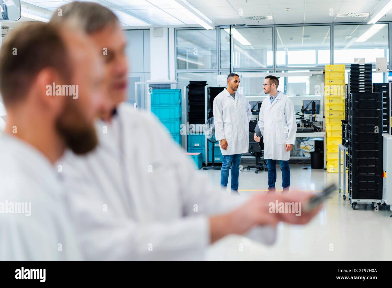Techniker in Elektronikfabriken diskutieren über das Motherboard, während Kollegen im Hintergrund sprechen Stockfoto