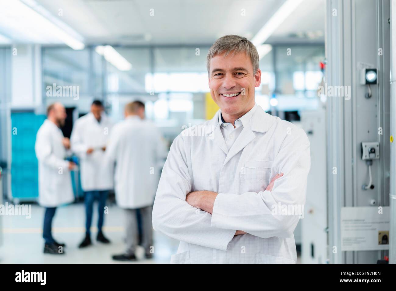 Techniker im weißen Labormantel, der in der Elektronikfabrik mit überkreuzten Armen steht Stockfoto