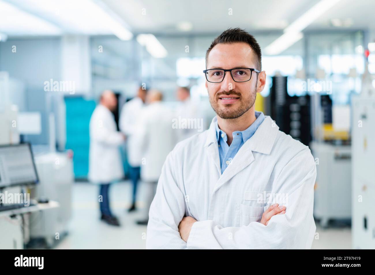 Selbstbewusster Elektrotechniker, der mit überkreuzten Armen in der Elektronikfabrik steht Stockfoto