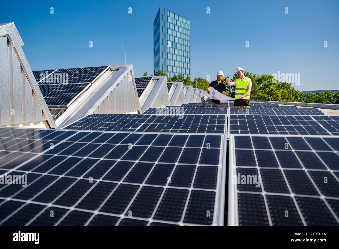 Zwei Techniker, die auf dem Dach eines mit Solarpaneelen ausgestatteten Firmengebäudes strategisch arbeiten Stockfoto