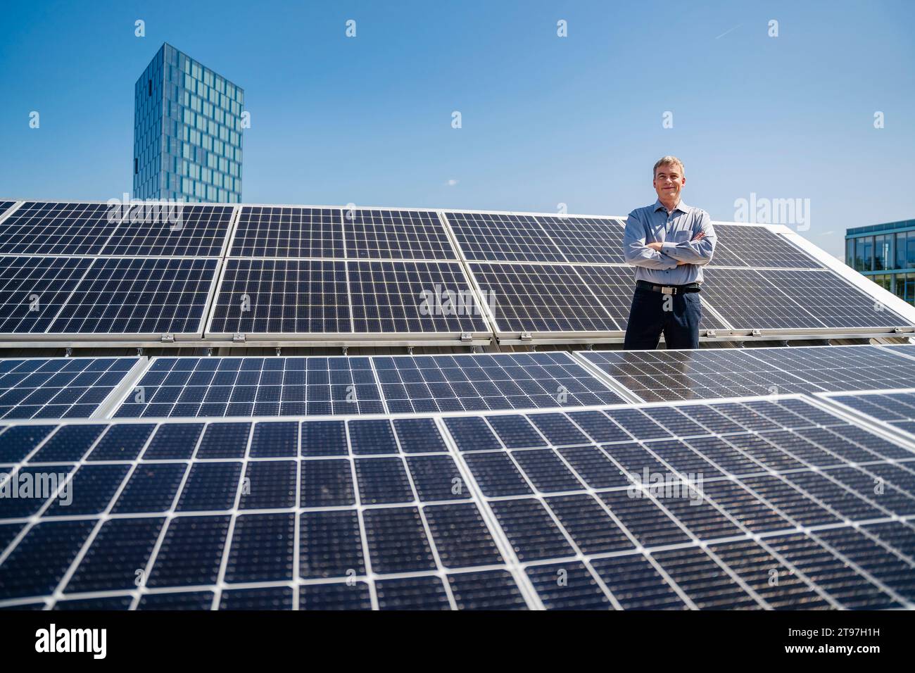 Ein selbstbewusster männlicher Unternehmer, der stolz inmitten eines Feldes von Solarpaneelen steht Stockfoto